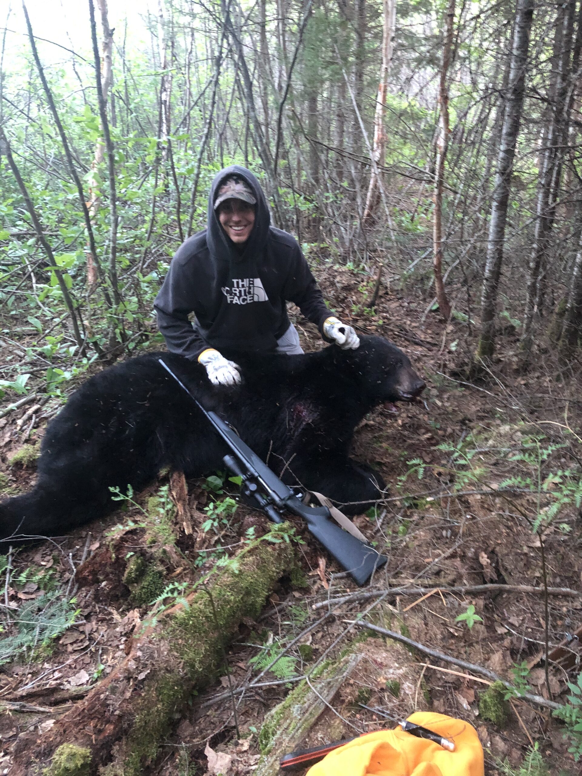 Chasseur Adam avec son fusil et un ours noir abattu au Québec – photo de chasse sur le terrain.